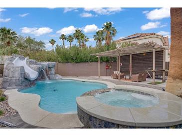 A backyard pool with a slide and waterfall feature and a lounge area under a pergola at 7621 Hackensack Ct, Las Vegas, NV 89128