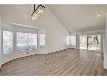 Bright living room featuring wood floors, high ceilings, a modern chandelier, and large windows providing ample natural light at 6944 Emerald Springs Ln, Las Vegas, NV 89113