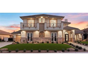 Elegant two-story home featuring dual balconies, stone accents, manicured lawn, and arched entryway at 9605 Verlaine Ct, Las Vegas, NV 89145