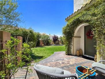 A quaint backyard with lush green grass and access to the home from a brick and stone tiled patio at 396 Blackstone River Ave, Las Vegas, NV 89148