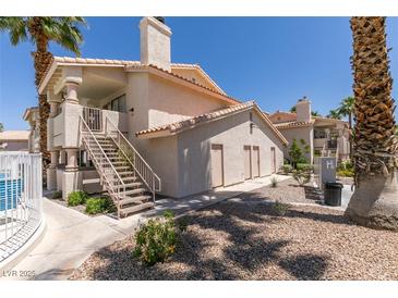 Condo building exterior with stairs, desert landscaping, and visible community pool at 1013 Falconhead Ln # 202, Las Vegas, NV 89128
