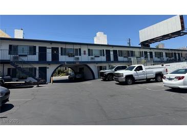 A white two-story building featuring exterior stairs and arched driveway entrance with parked trucks and cars at 4600 Paradise Rd # 16, Las Vegas, NV 89169