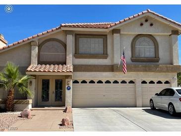 Two-story home featuring a three-car garage, an American flag, a desert landscape, and a tile roof at 4542 Amber Canyon Ln, Las Vegas, NV 89129
