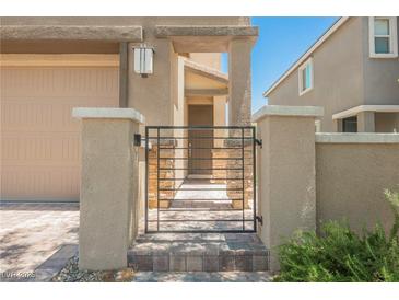 Front gate entry to a two-story home with beige stucco and a paver walkway leading to the front door at 920 Cirrus Cloud Ave, Las Vegas, NV 89138
