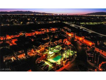 Night aerial view of a well-lit community with a pool and a distant city skyline at 1557 Blue Sierra Ct, Henderson, NV 89074