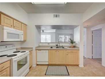 Well-lit kitchen featuring appliances, light wood cabinets, and a pass-through to the living area at 6955 N Durango Dr # 1093, Las Vegas, NV 89149