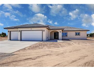 Charming single-story home featuring a three-car garage, arched entryway, and desert landscaping at 1131 Lupin St, Pahrump, NV 89048
