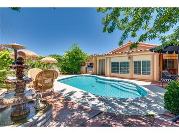 Inviting backyard pool with fountain, lush landscaping, and ample seating areas for outdoor relaxation at 3877 Platis Cir, Las Vegas, NV 89103