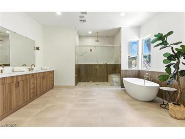This modern bathroom features a soaking tub, glass enclosed shower, and a wood vanity at 9408 Players Canyon Ct, Las Vegas, NV 89144