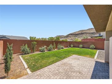 Well-maintained backyard with a brick patio, green lawn, and desert landscaping at 10693 Harvest Green Way, Las Vegas, NV 89135