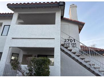 Exterior shot of a white two-story condo with stairs, a red tile roof and a small bush out front at 2701 Beaver Creek Ct # 201, Las Vegas, NV 89117