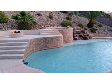 Resort-style pool with waterfall feature, fire pit, and lush landscaping creates a backyard oasis at 2197 Big Bar Dr, Henderson, NV 89052