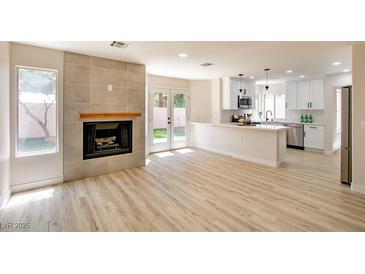 Bright living room with modern fireplace, light wood floors, and seamless access to a white kitchen and backyard views at 2204 Brighton Shore St, Las Vegas, NV 89128