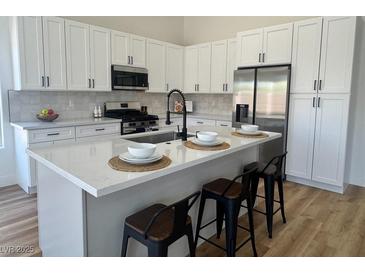 Bright kitchen features white cabinetry, stainless steel appliances, and a quartz countertop island with seating at 5600 Nimes Ave, Las Vegas, NV 89141