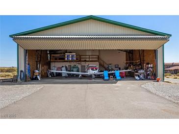 View of Airplane Hangar, concrete floor, with bi-fold door open, airplane inside, and storage shelves at 1100 Mitchell Pl, Pahrump, NV 89060