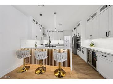Bright kitchen with white cabinets, quartz countertops, wood floors, and stylish barstool seating at the island at 9900 Summer Ash Ct # 103, Las Vegas, NV 89134