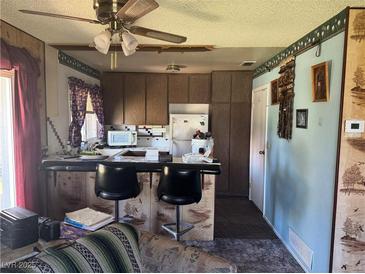A view of a kitchen with dark countertops, bar seating, and a ceiling fan with light at 1507 Elizabeth Ave # 1, Las Vegas, NV 89119