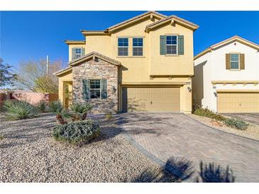 Two-story home featuring a stone facade, tan exterior, and a two-car garage with a brick paved driveway at 8992 Sparkling River Ct, Las Vegas, NV 89178