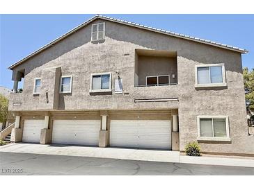 Condominium complex featuring stucco exterior, multiple garages, and a balcony against a clear blue sky at 2000 Gravel Hill St # 203, Las Vegas, NV 89117