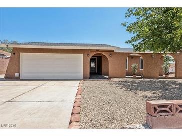 Charming single-story home featuring a two-car garage, an arched entryway, and desert landscaping at 667 Del Prado Dr, Boulder City, NV 89005