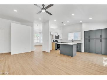 Bright, open-concept living space with light wood floors flowing into modern kitchen with island and stainless appliances at 831 Purple Sage Ter, Henderson, NV 89015