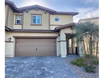 Two-story home with tan siding, brown trim, a two car garage, and a beautiful brick paver driveway at 302 Bay Village Pl, Henderson, NV 89011