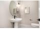 Elegant powder room featuring a pedestal sink, round mirror, modern lighting fixture, and separate toilet area at 7062 Maverick St, Las Vegas, NV 89131