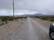 View down a long dirt road approaching a desert property with scattered vegetation under a cloudy sky at , Pahrump, NV 89060