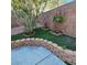 Landscaped backyard featuring stone accents, artificial turf, mature tree, and a concrete patio at 11261 Playa Caribe Ave, Las Vegas, NV 89138