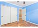 Blue bedroom with wood floors, closet, ceiling fan, and open doorway to another room at 1053 Plentywood Pl, Henderson, NV 89002