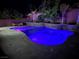 Inviting in-ground pool illuminated with vibrant blue lighting and complemented by a stone waterfall feature and lush landscaping at 5873 Skyfall Ct, Las Vegas, NV 89135