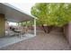 An outdoor patio with a table and chairs and a gravel yard with a mature shade tree at 4920 Blue Rose St, North Las Vegas, NV 89081