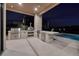 An outdoor kitchen includes a grill, pizza oven, refrigerator, and a covered patio with a pool view at night at 37 Reflection Shores Ln, Henderson, NV 89011