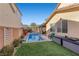 Landscaped backyard with a pool, spa, artificial grass, and a view of the home's exterior under a clear blue sky at 10729 Beecher Park Ave, Las Vegas, NV 89166