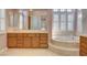 Well-lit bathroom featuring a large tub, double sinks, and wood cabinets at 29 Desert Highlands Dr, Henderson, NV 89052