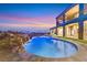 Beautiful in-ground pool with stone waterfall features and lush landscaping with a skyline sunset view at 5790 Aspen Falls Cir, Las Vegas, NV 89149