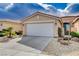 Beige home featuring a two-car garage, rock landscaping and mature trees at 5201 Progresso St, Las Vegas, NV 89135