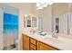 Bright bathroom featuring double sinks, wood cabinets, a large mirror, and a shower with a decorative blue curtain at 5130 Agio Ave, Pahrump, NV 89061