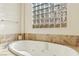 Close up of a soaking tub with jets featuring marbled tile surround and a glass block window at 12 Oro Valley Dr, Henderson, NV 89052