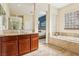 Spacious bathroom featuring a double mirror, wooden cabinets, and a soaking tub with marbled tile surround at 12 Oro Valley Dr, Henderson, NV 89052