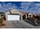 Front view of a tan stucco house with tile roof, two-car garage, and desert landscaping at 9900 Rosamond Dr, Las Vegas, NV 89134