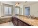 Bright bathroom featuring dual sinks, granite countertops, a soaking tub, and windows at 217 Via Luna Rosa Ct, Henderson, NV 89011