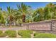 Welcoming stone sign at Tuscany Village and Golf entrance, surrounded by lush greenery and swaying palm trees under a bright sky at 217 Via Luna Rosa Ct, Henderson, NV 89011