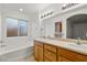 Bright bathroom featuring double sinks, a window over the tub, and wood cabinets for ample storage at 210 Bristle Cone, Pahrump, NV 89048