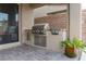 Outdoor kitchen with built-in grill, granite counters, stainless steel storage, and brick accent wall at 10936 White Alder Pl, Las Vegas, NV 89138