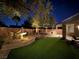 Landscaped backyard features mature trees, a water fountain, synthetic grass and brick accents under ambient landscape lighting at 6886 Barred Dove Ln, North Las Vegas, NV 89084