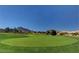 A well-maintained golf course with a green and a flag, framed by mountains and clear blue skies at 2540 Youngdale Dr, Las Vegas, NV 89134