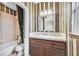 A cozy bathroom featuring a shower-tub combination and a single sink vanity with warm, striped wallpaper at 25 Via Mantova # 2, Henderson, NV 89011