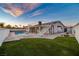 A beautiful backyard features a refreshing pool, green lawn, and a unique second-story deck at sunset at 6255 Adenmoor Ct, Las Vegas, NV 89156