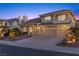 Charming two-story home with a tile roof, a three-car garage, a paved driveway, and lush, mature landscaping at dusk at 4439 Melrose Abbey Pl, Las Vegas, NV 89141